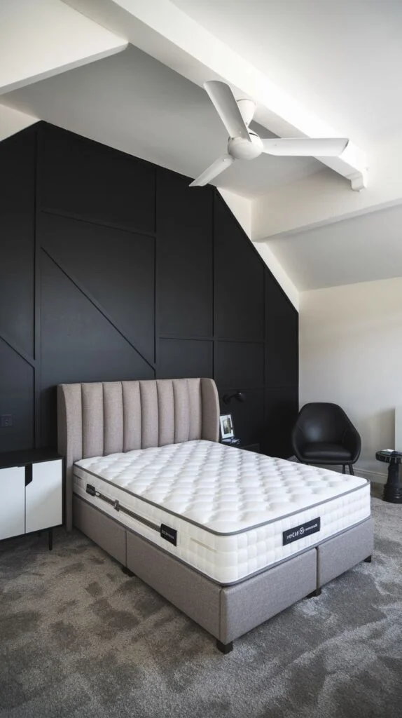 Black accent wall with large asymmetrical panels fitting a sloped ceiling behind a gray upholstered bed