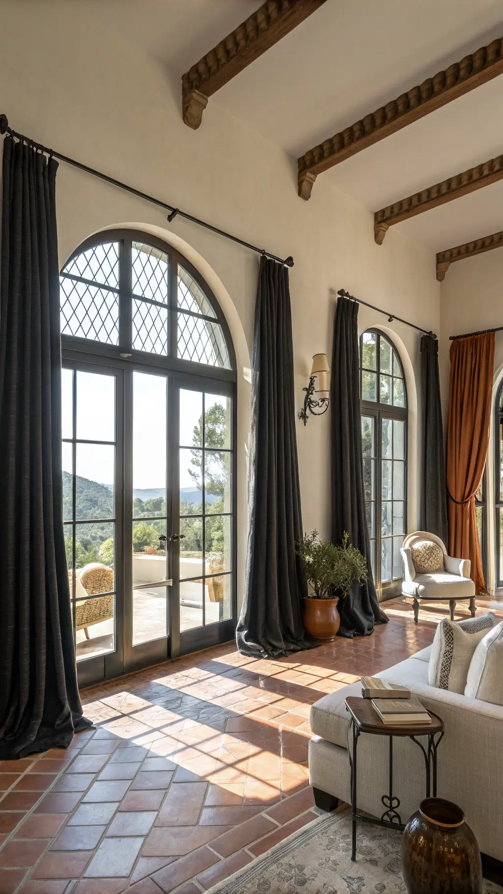 Mediterranean-modern styled great room with cream upholstery, black iron accents, terracotta and brass accessories, linen curtains framing arched windows illuminated by natural light.