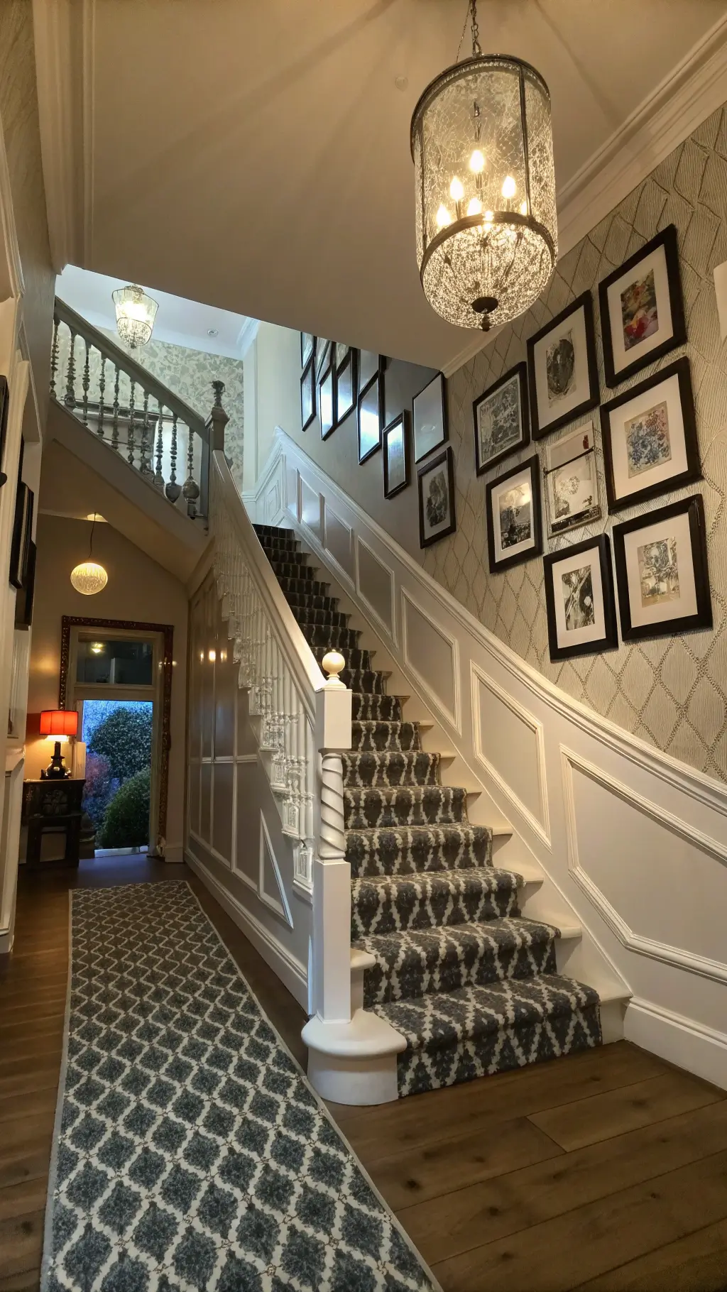 Victorian entryway with grand staircase, modern geometric runner, abstract art gallery wall, white wainscoting, metallic damask wallpaper, vintage chandelier with updated LED bulbs, dramatic lighting