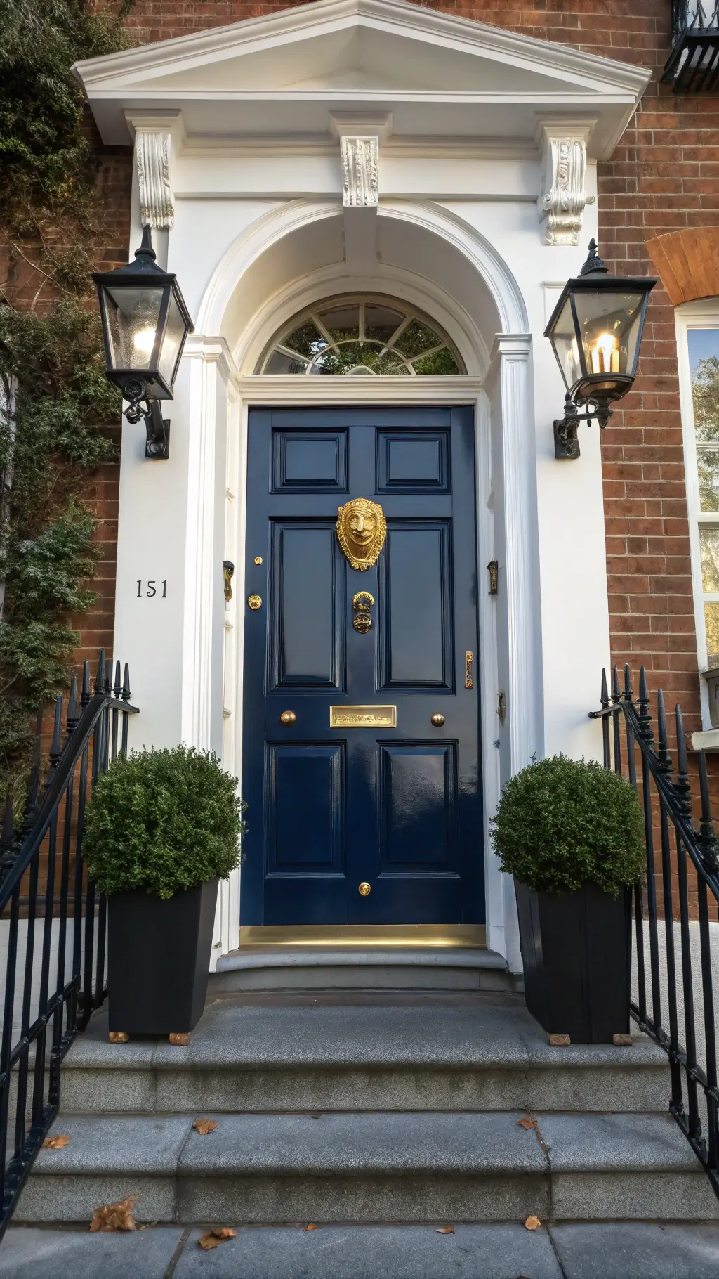 Classic Georgian entrance with high-gloss navy door, brass lion knocker, white dental molding, boxwood topiaries in black planters, and Belgian bluestone steps in morning light
