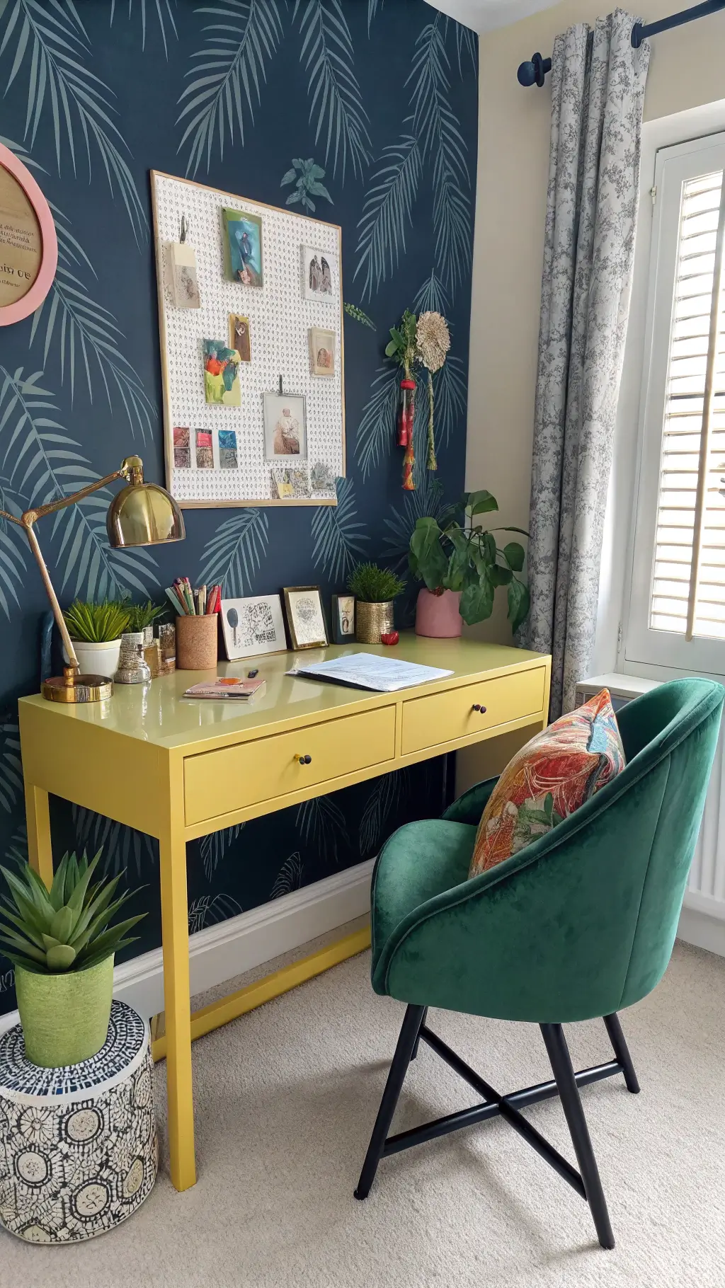 Maximalist bedroom workspace with chartreuse yellow desk, navy tropical palm wallpaper, rose gold accessories, succulent plants in colorful ceramic pots, emerald green velvet task chair, and circular pin board under morning window light.
