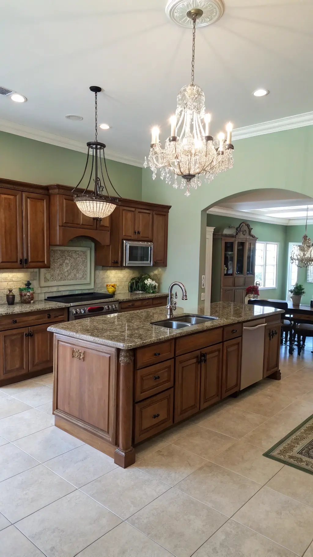 Traditional open-concept kitchen with red oak cabinets, cream granite countertops, sage green walls, and a crystal chandelier