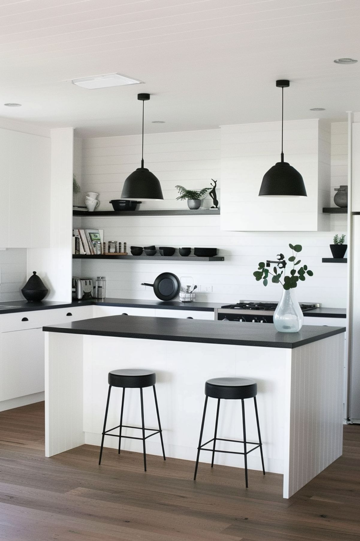 Minimalist kitchen with white island, black countertops, and black pendant lights.