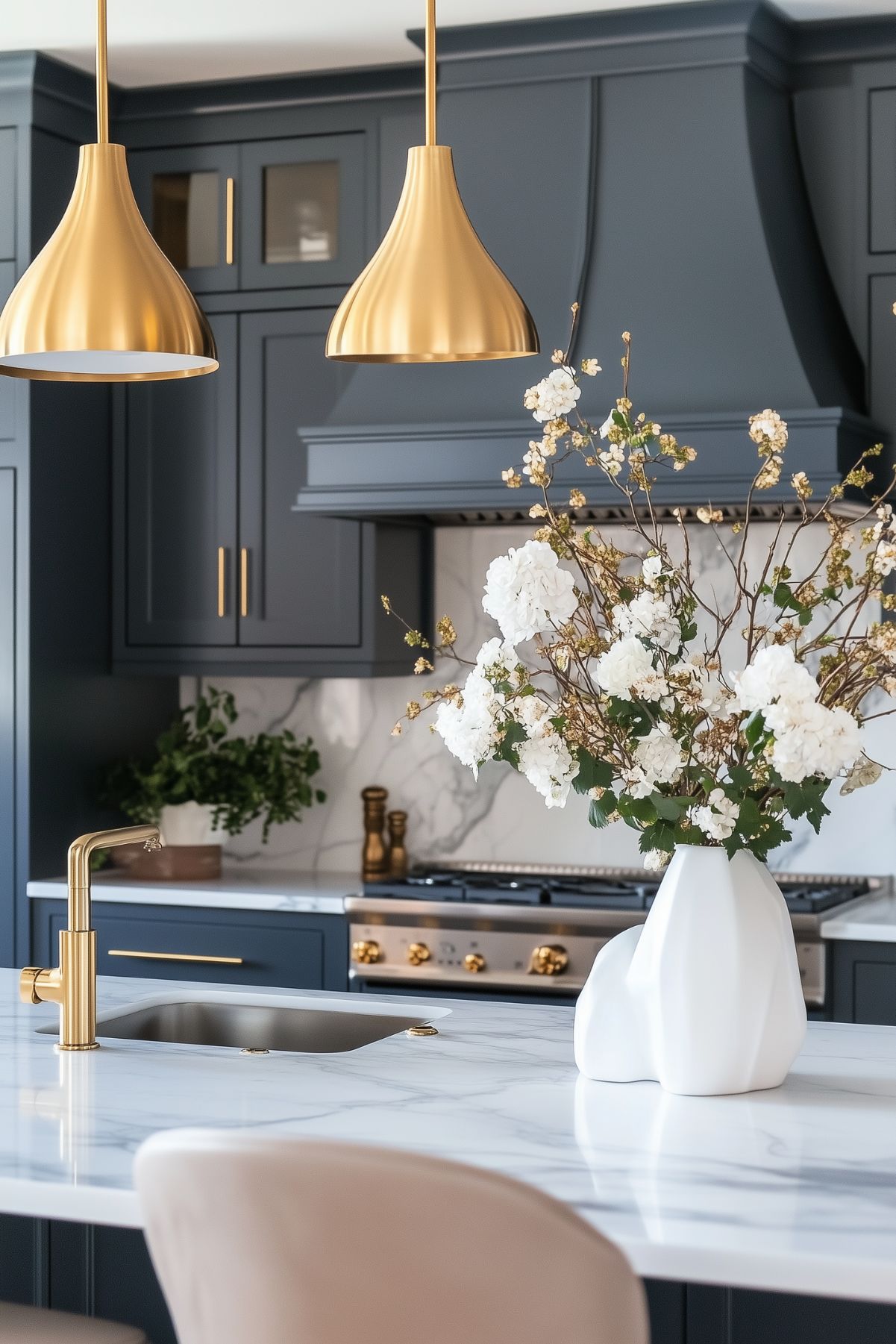 Modern kitchen with blue-gray cabinets, gold pendant lighting, marble countertops, and a gold faucet centerpiece.