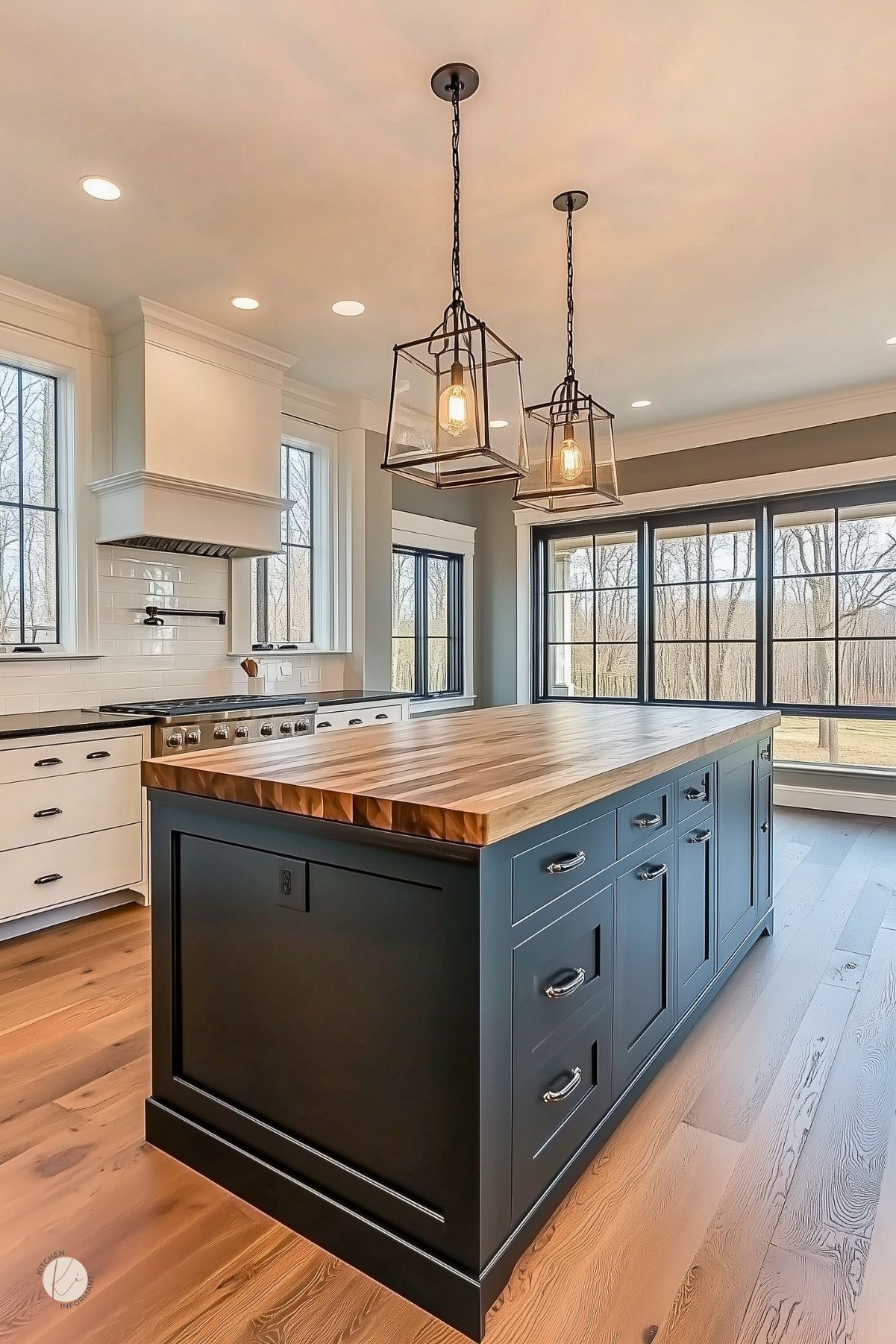 Modern kitchen with a navy blue island featuring a butcher block countertop, white cabinetry, subway tile backsplash, and large windows. Black lantern pendant lights add a rustic touch above the island.