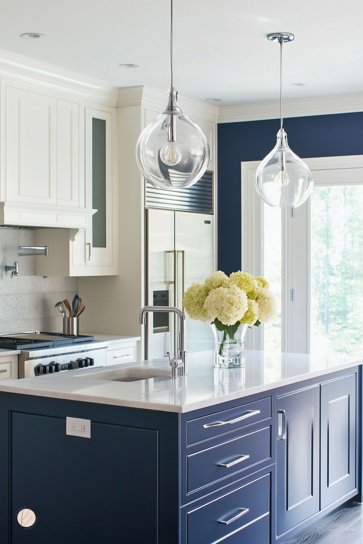 Contemporary kitchen featuring a navy blue island with a marble countertop, stainless steel appliances, and white cabinetry. Glass pendant lights and a vase of hydrangeas add a fresh, modern touch.